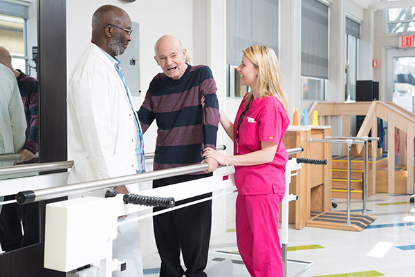 doctor and therapist helping elderly man walk